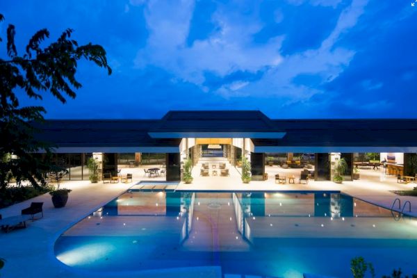 A luxurious pool area is shown with modern architecture and ambient lighting under a twilight sky, highlighting a serene and inviting atmosphere.