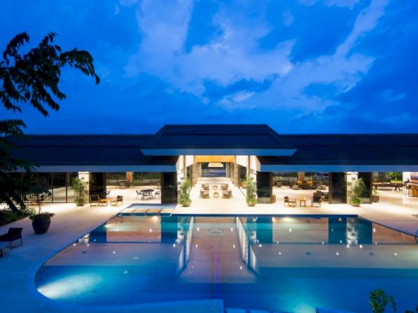 A luxurious pool area is shown with modern architecture and ambient lighting under a twilight sky, highlighting a serene and inviting atmosphere.