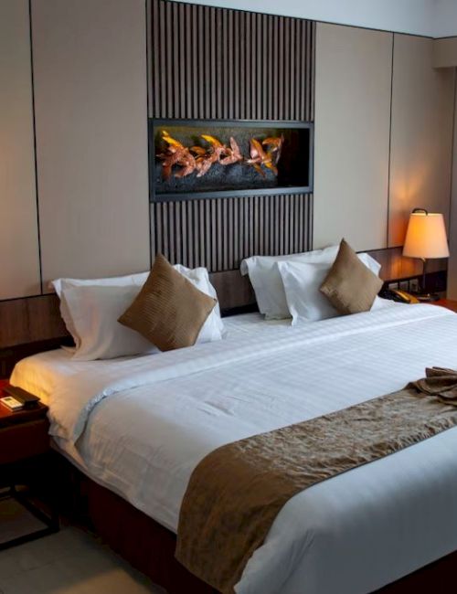 A neatly arranged hotel room features a large bed with white linens, brown accents, bedside lamps, and a modern wall decoration above the bed.