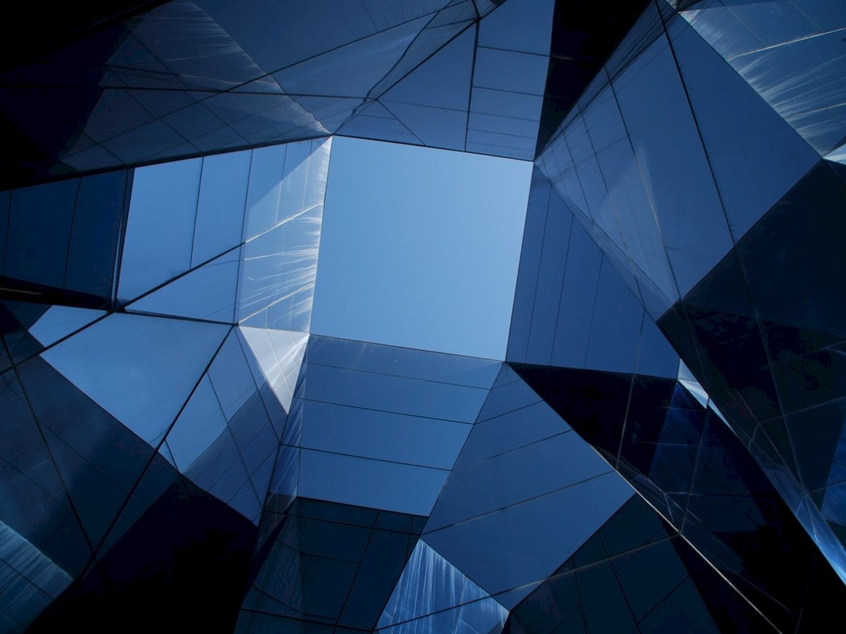 The image shows abstract architecture with reflective glass panels forming geometric patterns and creating an open sky view in the center.
