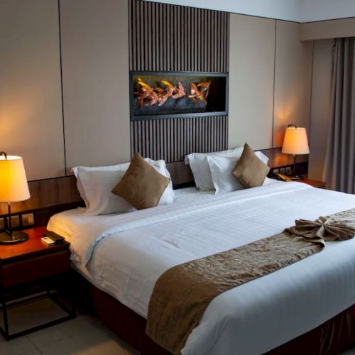 A modern hotel room with a large bed, lamps on bedside tables, and a decorative wall panel above the headboard. Curtains are partly drawn.