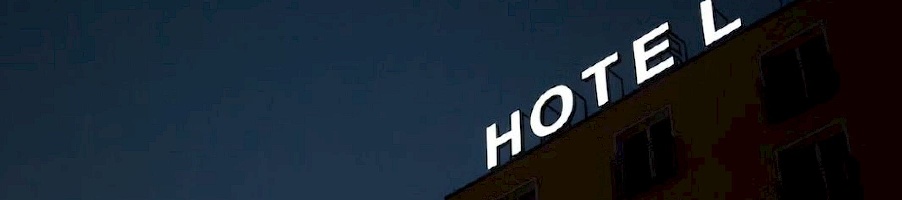 The image shows a building at night with a sign that reads "HOTEL." The "H" in "HOTEL" is partially not illuminated.