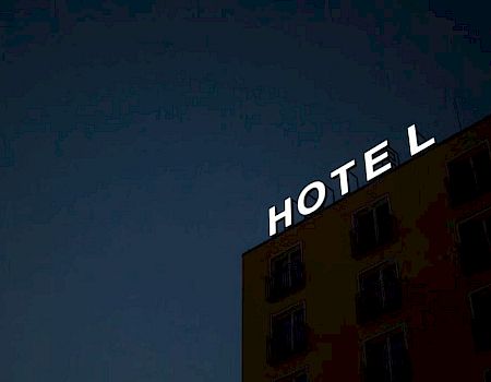 The image shows a building at night with a sign that reads "HOTEL." The "H" in "HOTEL" is partially not illuminated.