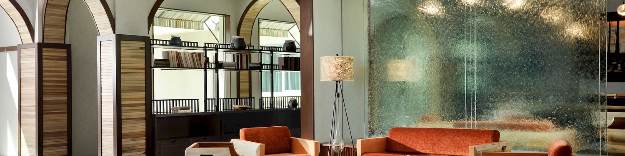 Modern lounge with archways, textured glass wall, and earthy furniture. Pendant lights add warmth to the contemporary setting.