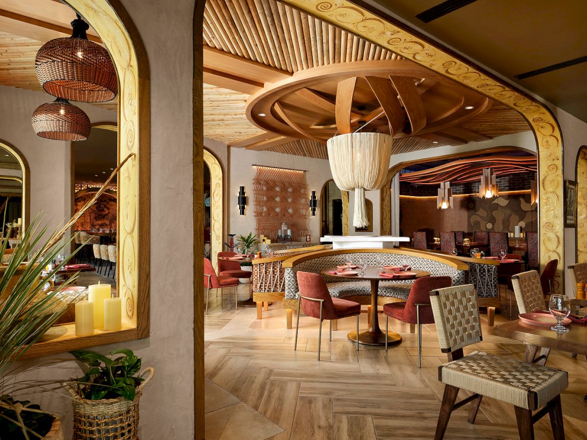 The image shows a stylish restaurant interior with wooden accents, woven chairs, cylindrical lights, and a cozy, inviting atmosphere.