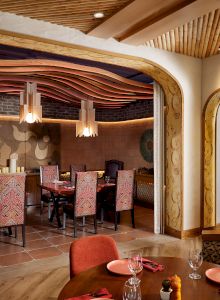 The image shows a stylish restaurant interior with patterned chairs, wooden accents, and decorative lighting, creating a cozy ambiance.