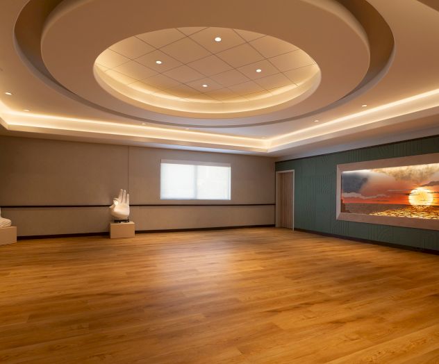 A serene room with wooden flooring, a Buddha statue, a hand sculpture, and a sunset ocean landscape on the wall is shown.