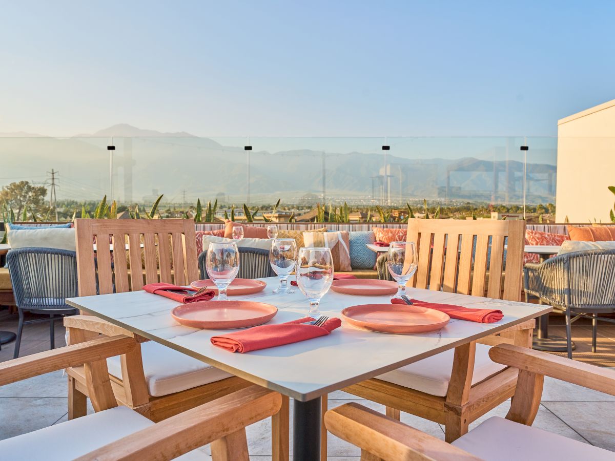 A rooftop restaurant setup with a table for four, set with plates, glasses, and napkins, offering a scenic mountain view.