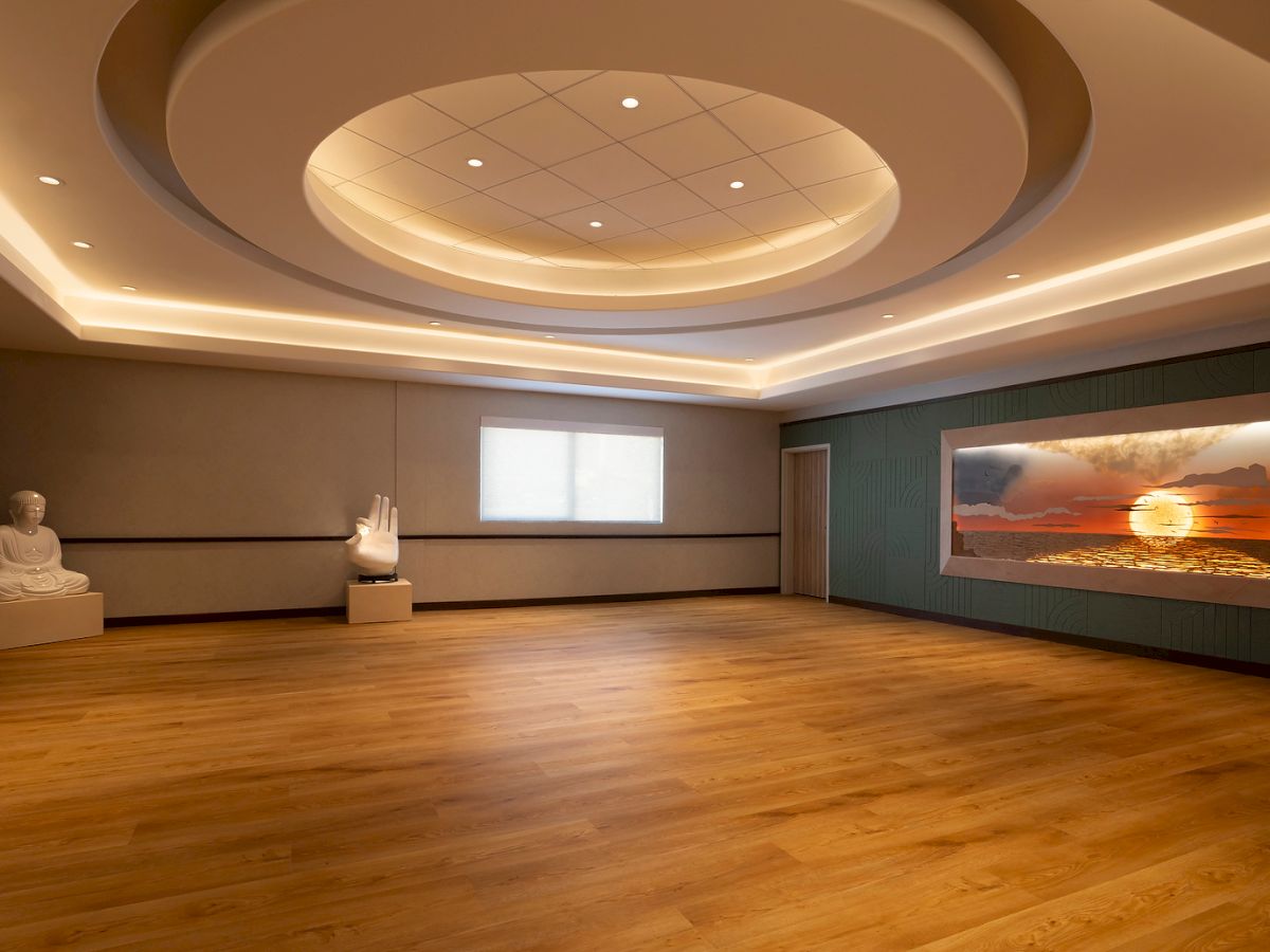 A serene room with a wooden floor, Buddha statue, large hand sculpture, and a wall display of a sunset over the ocean, under soft lighting.