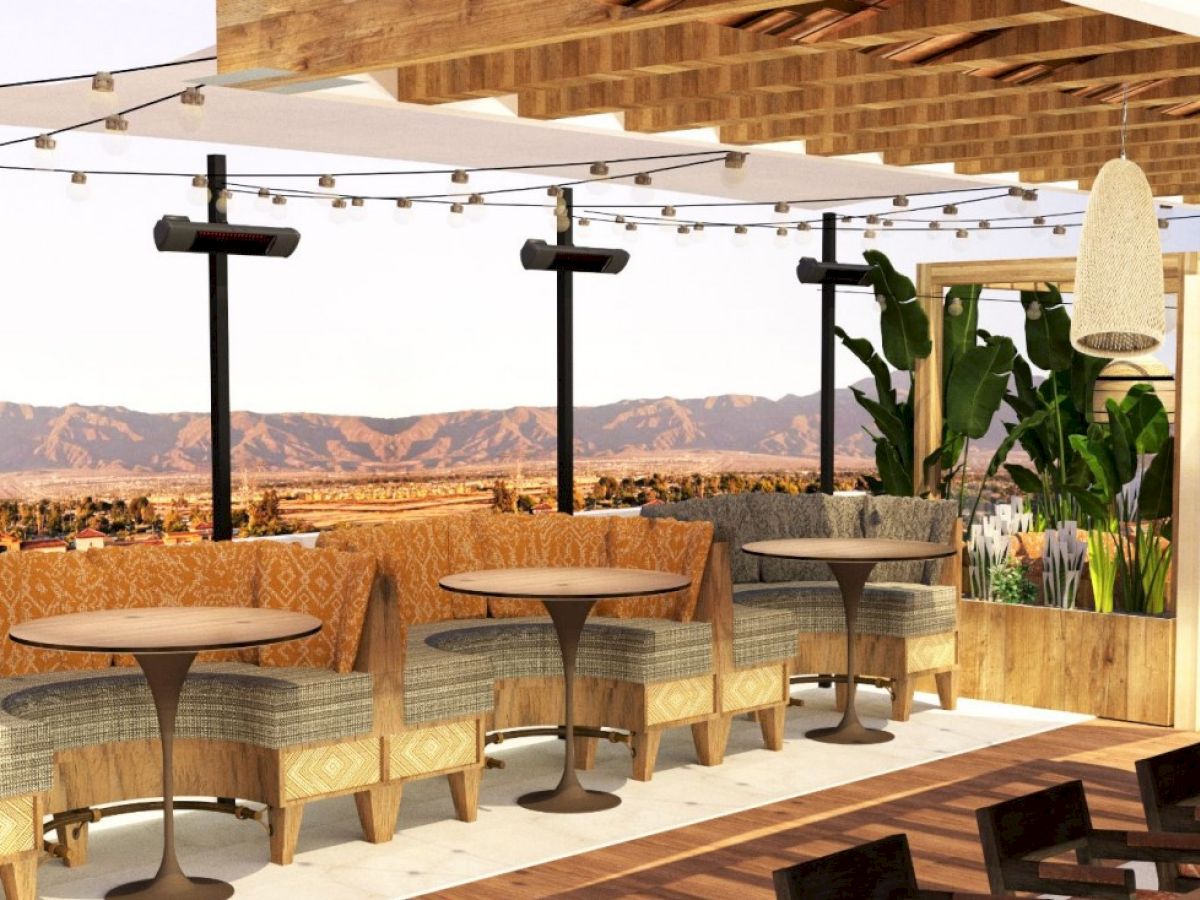 A stylish rooftop patio with cozy seating, tables, plants, and mountain views, featuring hanging lights and wooden accents, perfect for relaxation.