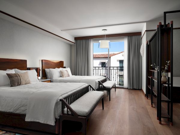 The image shows a hotel room with two beds, wooden furniture, a balcony, and modern decor.