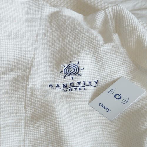 A white textured shirt with a &ldquo;Sanctity Hotel&rdquo; logo and a small tag that says &ldquo;Cairn&rdquo; on it, both placed on the fabric.