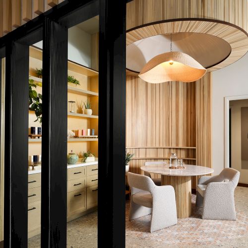 A stylish room with a round table, modern chairs, and a unique ceiling design. Wooden shelves hold decor items and plants, adding warmth.