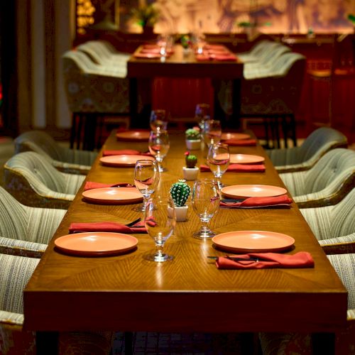 A well-set dining table with chairs, plates, glasses, and napkins in a cozy restaurant setting, featuring warm lighting and decor.