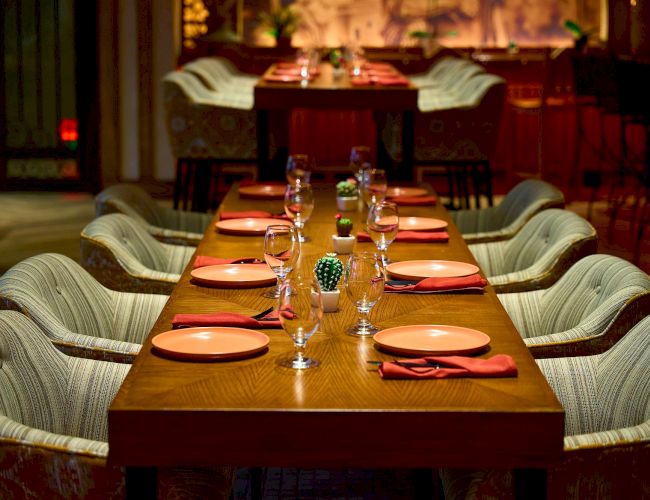 A well-set dining table with chairs, plates, glasses, and napkins in a cozy restaurant setting, featuring warm lighting and decor.