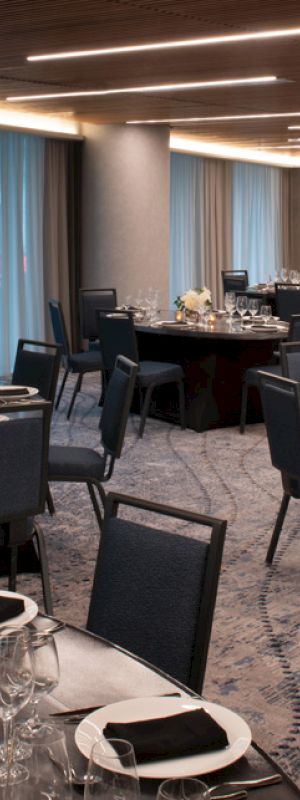 The image shows an elegantly decorated dining room with multiple round tables set with black napkins, glassware, and small floral centerpieces.