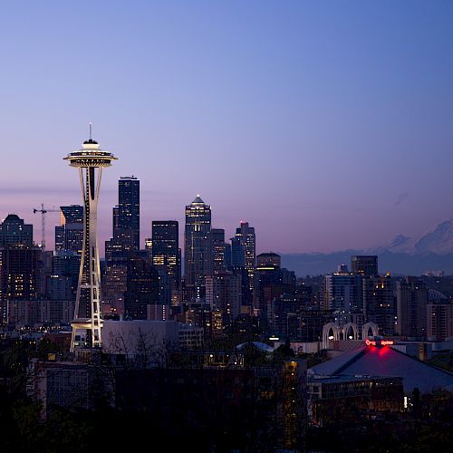 This image shows the Seattle skyline at dusk, featuring the Space Needle prominently, with downtown buildings and Mount Rainier visible in the background.
